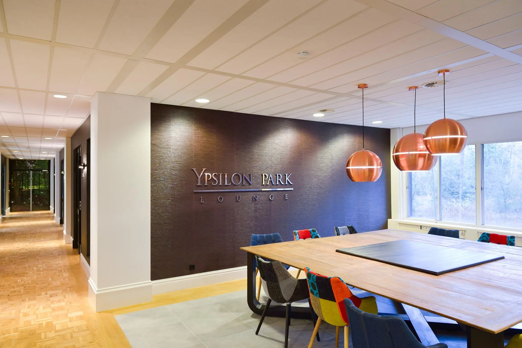 Moderne vergaderruimte in de Ypsilon Park Lounge met kleurrijke stoelen, houten tafel en koperen hanglampen.